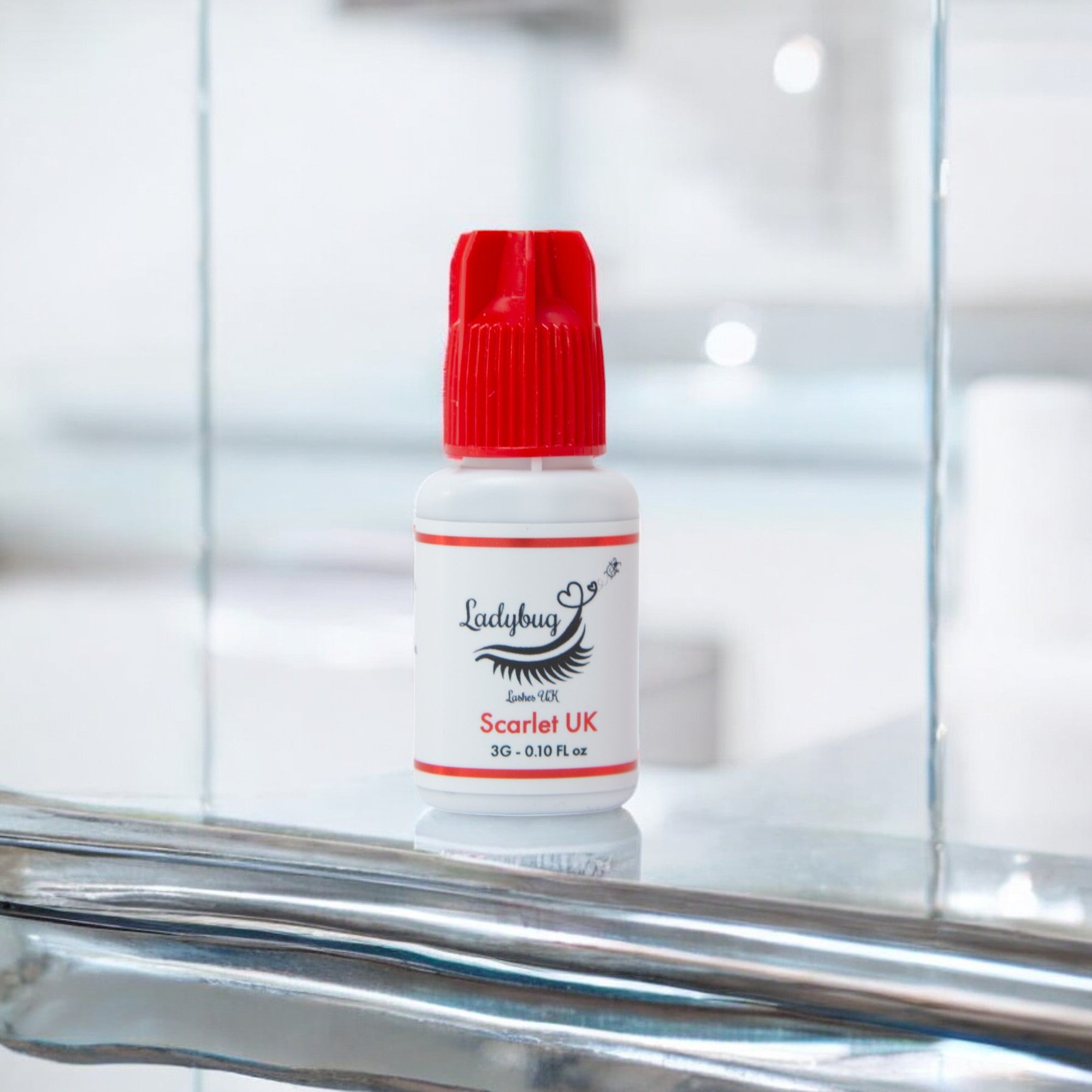 A bottle of Scarlet UK 1-2 Second adhesive/glue with a red cap on a reflective surface, labeled for eyelash extensions.