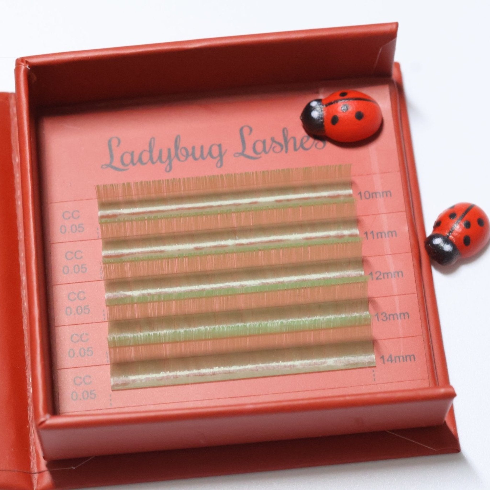 Ladybug Lashes Colour Volume Lashes 0.05mm open tray product shot showing multiple rows of mint green volume lash extensions in mixed lengths 10–14mm in a red Ladybug Lashes branded lash tray with ceramic ladybug figurines from diagonal angle on white background