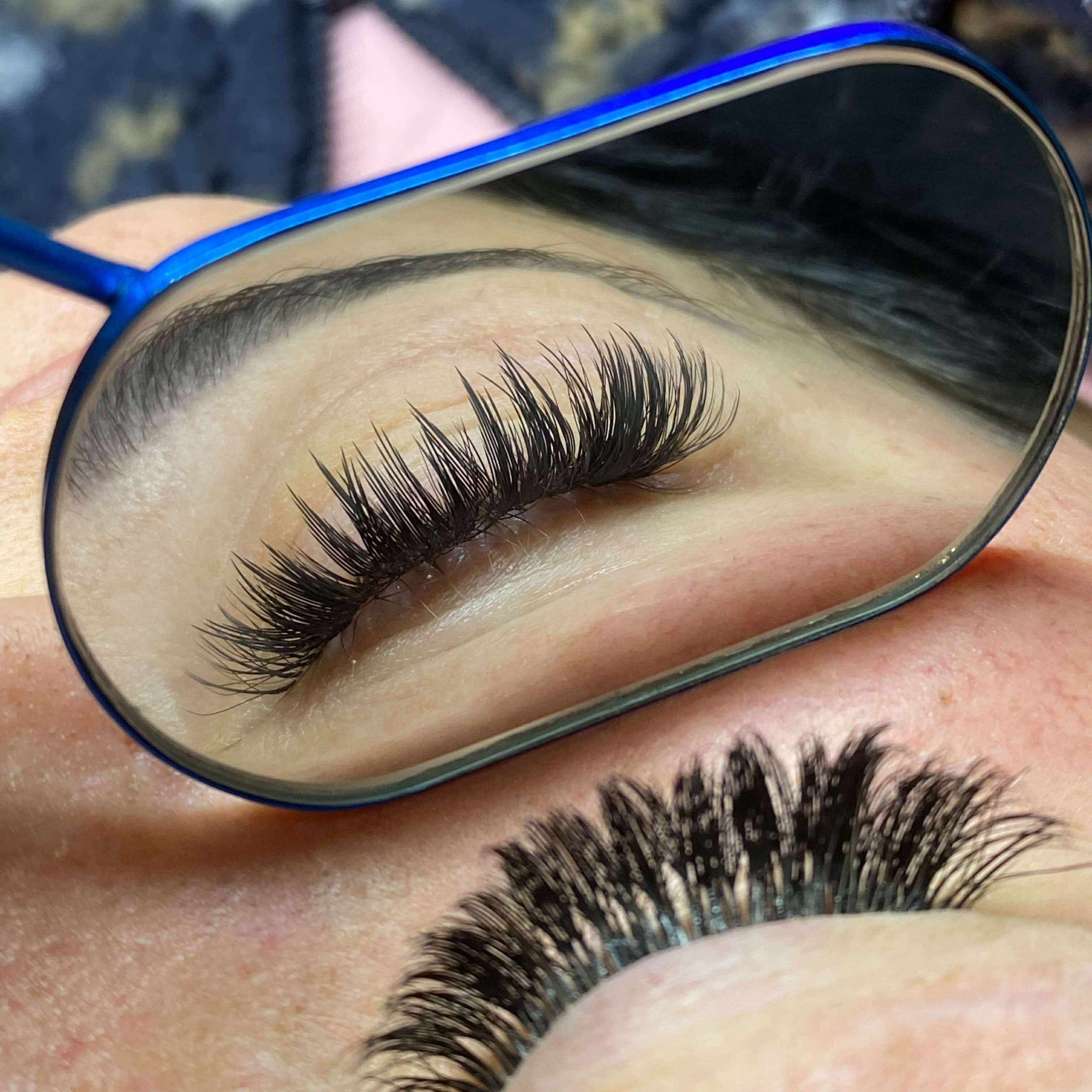 Overhead close-up of Anime Feather lash extension set on blue-grey eyes showing dramatic feather spike volume and wispy separation on both eyes mirror view