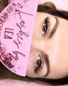Close-up of a person's eyes with a pink makeup product in the foreground.