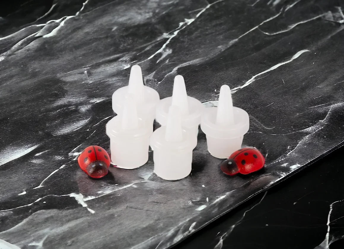 A set of clear plastic replacement nozzles for adhesive bottles, displayed on a marble surface with a few red adhesive dots visible.