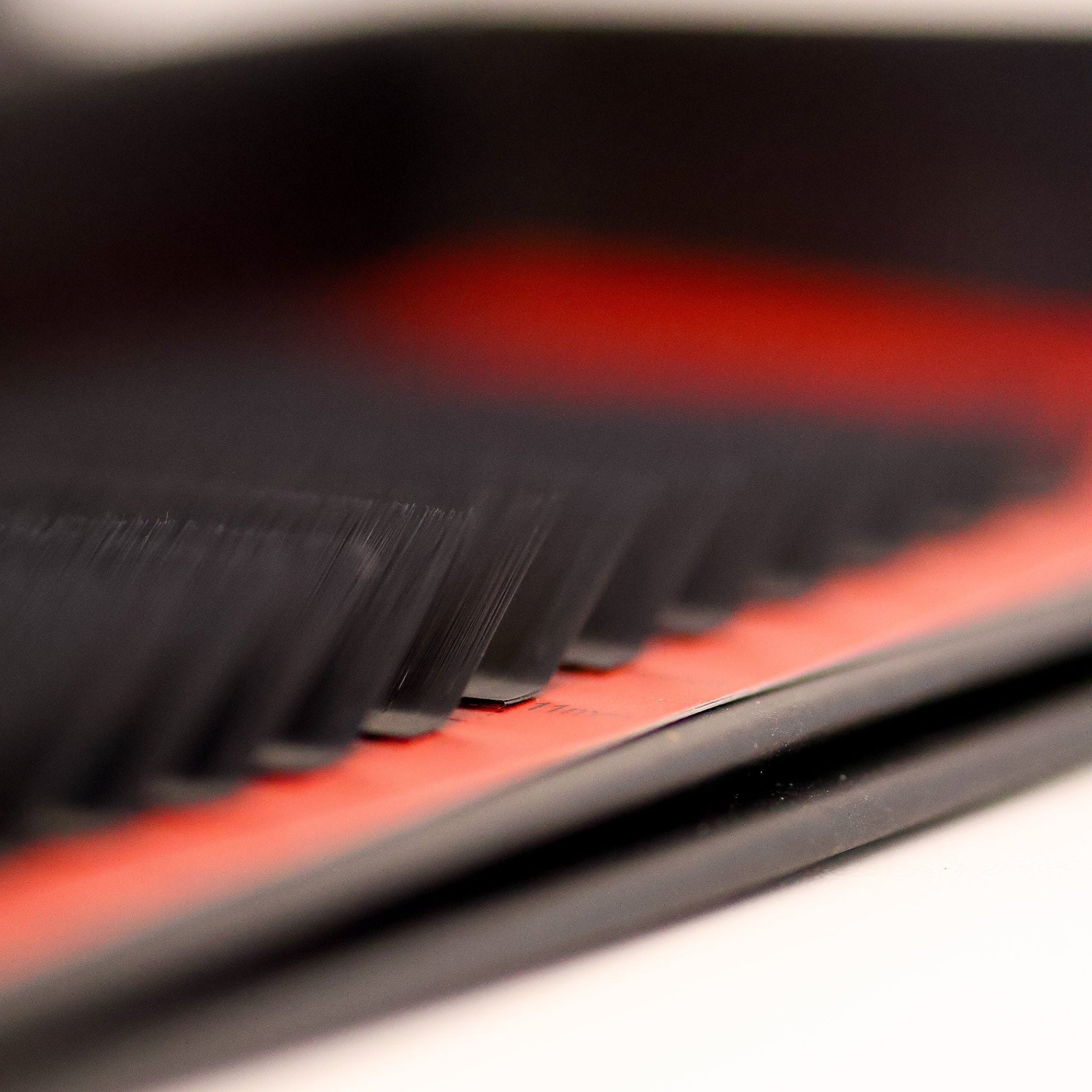 Ultra close-up side view of L curl lash extensions on red Ladybug Lashes tray showing flat bases and sharp L curl angle from low angle