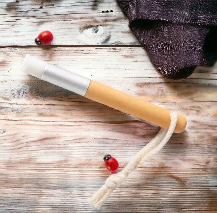 A beige bamboo lash shampoo brush with a white sponge tip, laying on a wooden surface, with some eyelashes and a spoolie brush in the background.