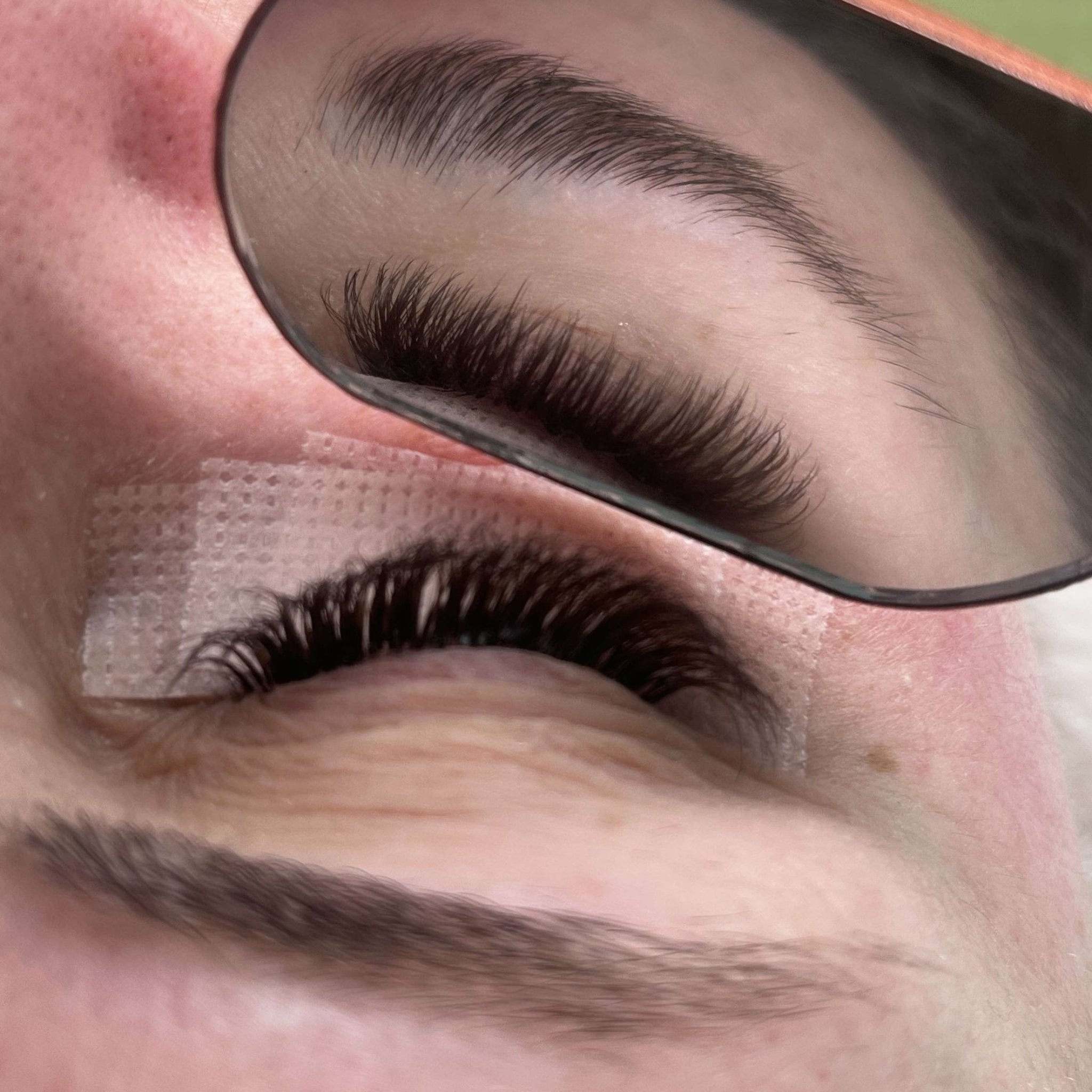 Lash technician applying brown Fairy lash extensions with mirror tool showing isolation technique and natural lash separation during treatment