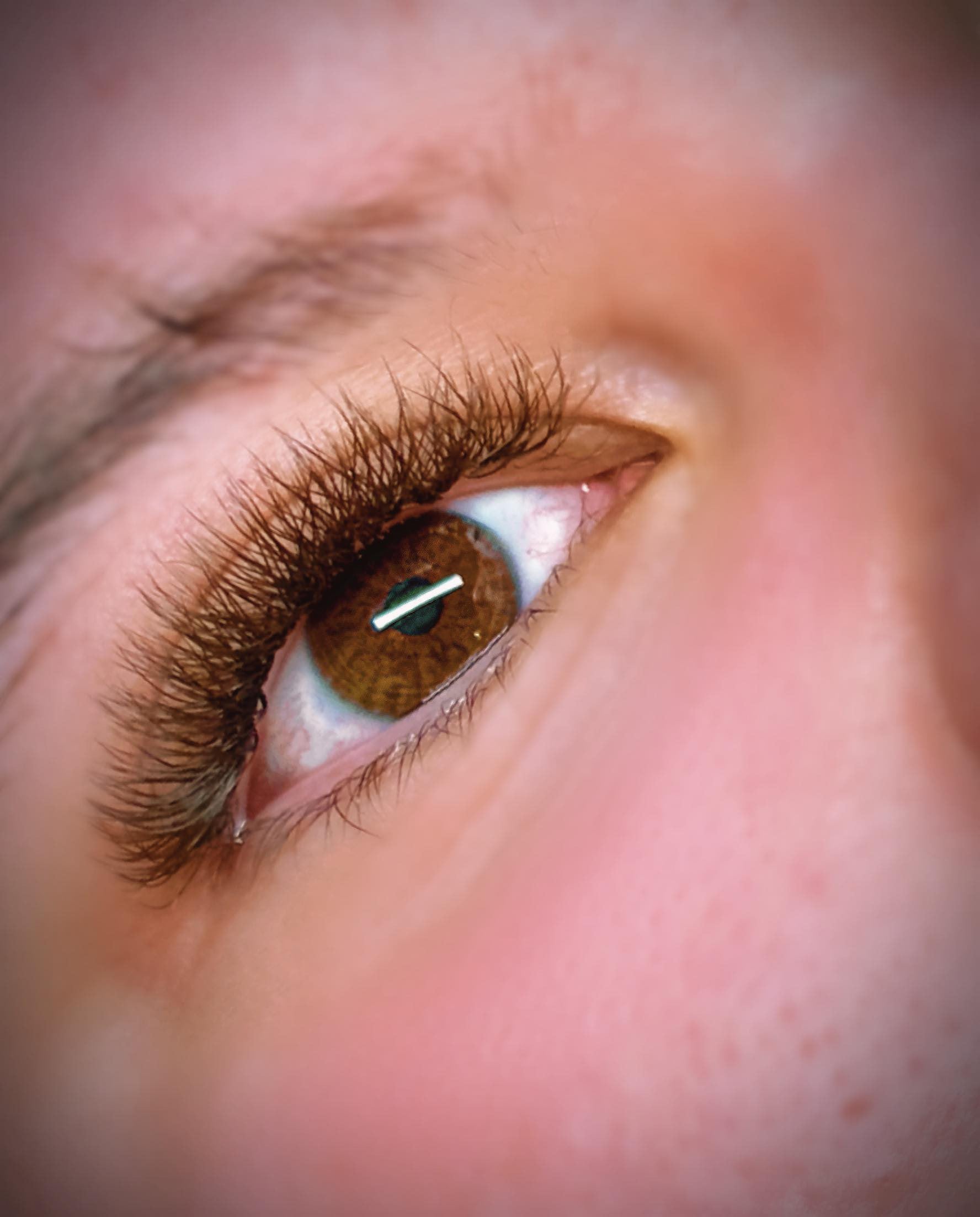 Close-up of an eye with brown false eyelashes applied, showcasing the length and curl of the lashes.