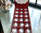 A display box containing 18 bottles of lash shampoo, with the product label 'Lash Shampoo Bubble Gum' on the top. The box is presented on a table with a floral decoration in the background.