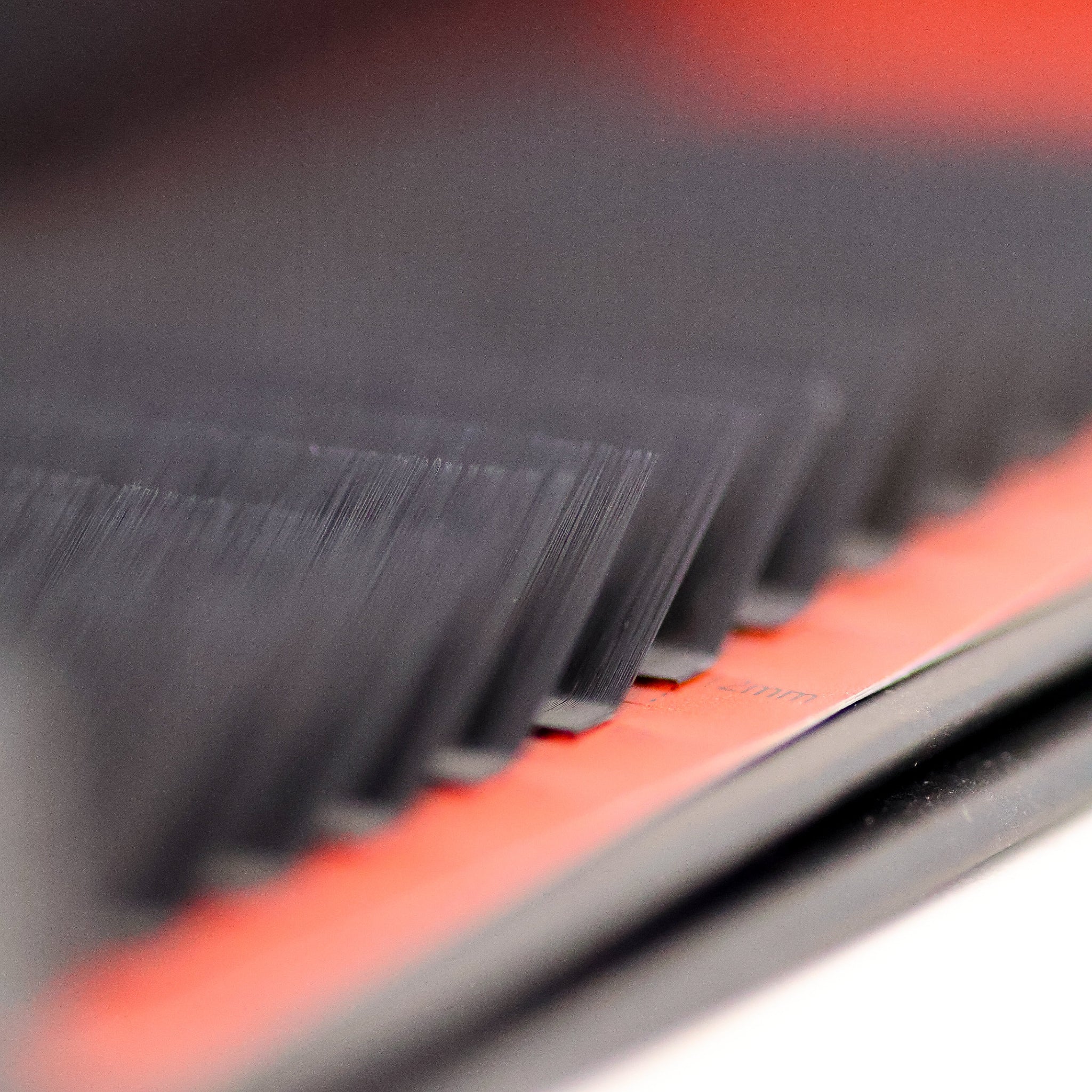 Extreme macro side-angle close-up of L curl lash extensions on red Ladybug Lashes tray showing flat base and distinctive L-shaped curl structure