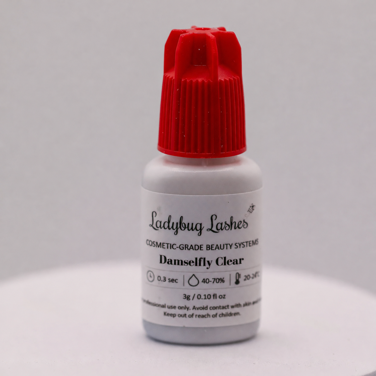 Ladybug Lashes Damselfly Clear lash adhesive 5g bottle with red cap showing product label with 0.3 sec bond time, 40–70% humidity range, 20–24°C temperature range and cosmetic-grade beauty systems branding on white background
