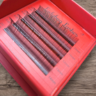 Red box containing false eyelashes with 'Ladybug Lashes' branding on a wooden surface.
