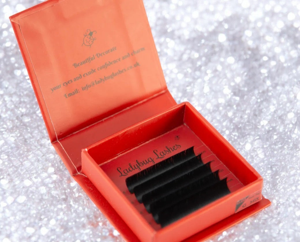 A close-up image of a person's eyelash extension application in progress, with a specific focus on the lashes and a lash extension tool being used.