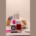 Ladybug Lashes Flutter and Frame Airless Pump Lash Lift Kit flatlay showing three Ladybug Lashes Flutter and Frame Step One Two Three airless pump bottles on a white plinth, pink Y-shaped silicone lifting tool, red Ladybug Lashes branded box, pink silicone under-eye patches, white lash shampoo bottle, coloured mascara spoolies, wooden spatulas, lash lifting rod, fine detail brushes and cotton buds on a white surface