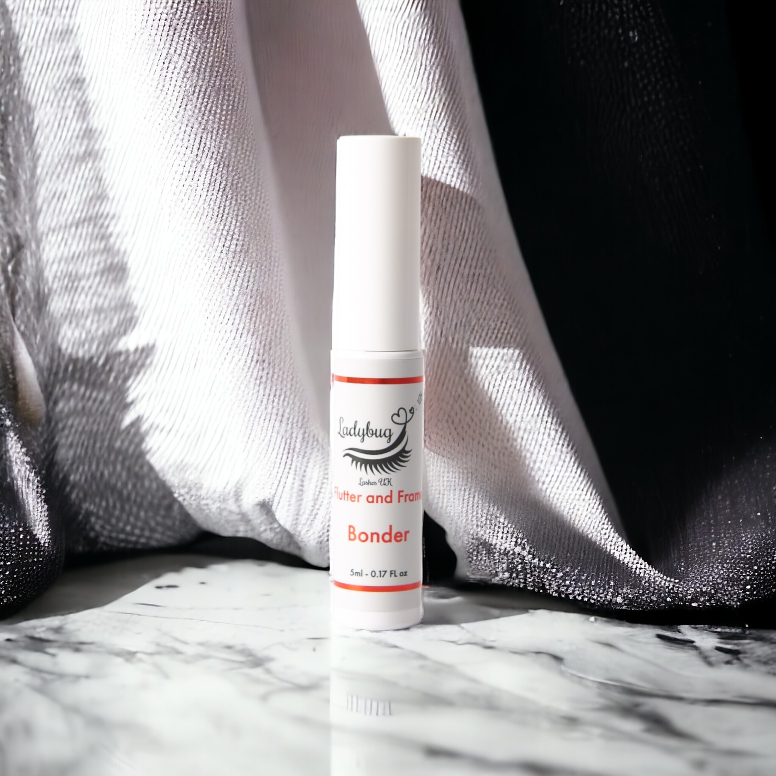 A bottle of Lash lift Adhesive/Bonder placed on a marble surface with a white and black object in the background.