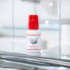 A bottle of Meadow UK 1-2 Second adhesive/glue with a red cap on a reflective surface, branded for Ladybug Lashes.
