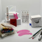 Ladybug Lashes Lash Lift Kit flatlay showing full kit contents including three Flutter and Frame Express Cysteamine treatment bottles, lash shampoo foam pump, coloured mascara wands, wooden spatulas, cotton buds, metal lash rod tool, white silicone lash shields, white medical tape roll and Ladybug Lashes branded cotton pad case on a white circular plinth on white background
