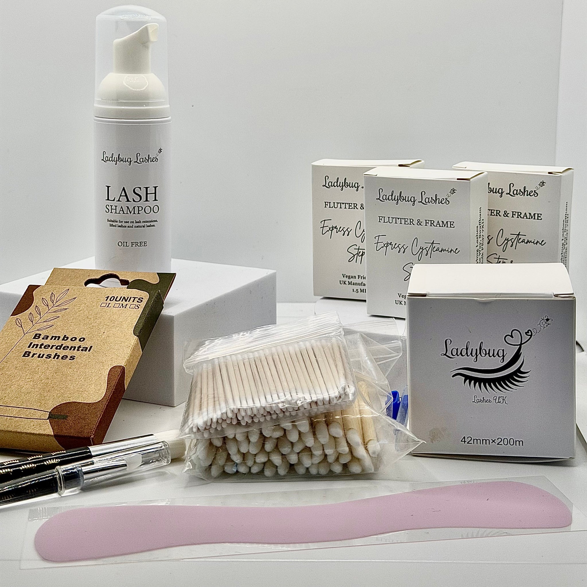 Ladybug Lashes Express Cysteamine Brow Lamination Sachet Kit flatlay showing Ladybug Lashes Lash Shampoo foam pump, three Flutter and Frame Express Cysteamine sachet boxes, Ladybug Lashes 42mm x 200m brow lamination wrap box, bamboo interdental brushes pack, cotton buds, microfibre brushes and pink silicone spatula on white background
