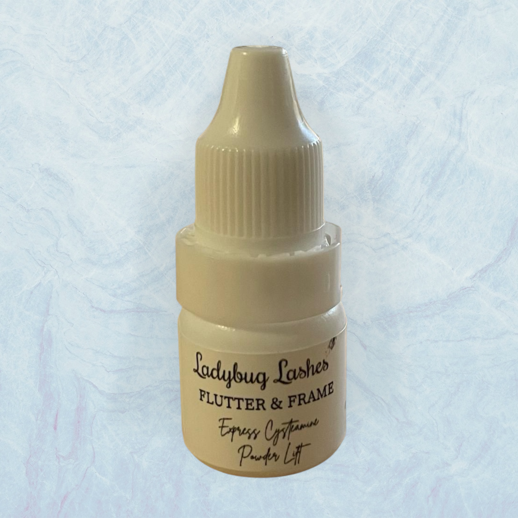 Small beige bottle labeled 'Ladybug Lashes Flutter & Frame' on a light blue textured background