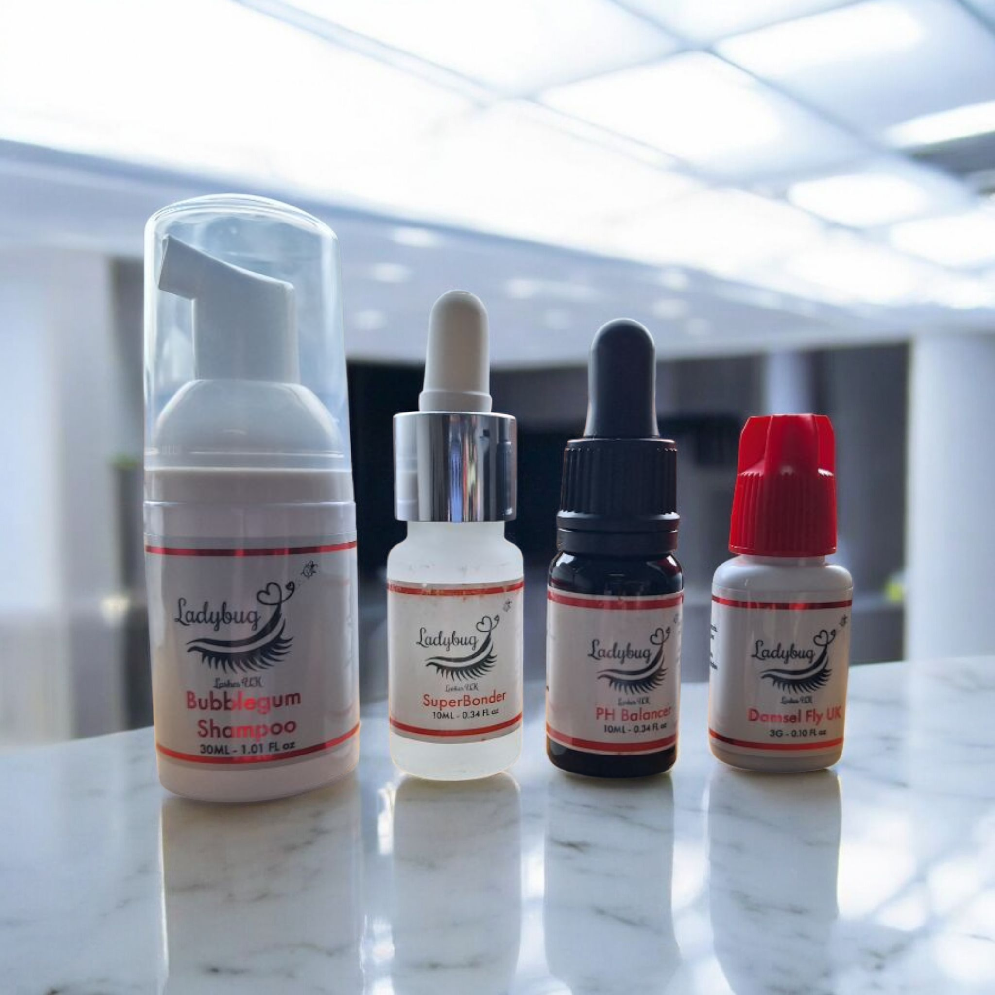 A collection of four cosmetic products on a light-colored surface, including a lash shampoo, ph balancer, glue, and superbonder, all labeled with the brand Ladybug Lashes.