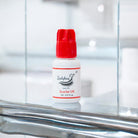 A bottle of Scarlet UK 1-2 Second adhesive/glue with a red cap on a reflective surface, labeled for eyelash extensions.
