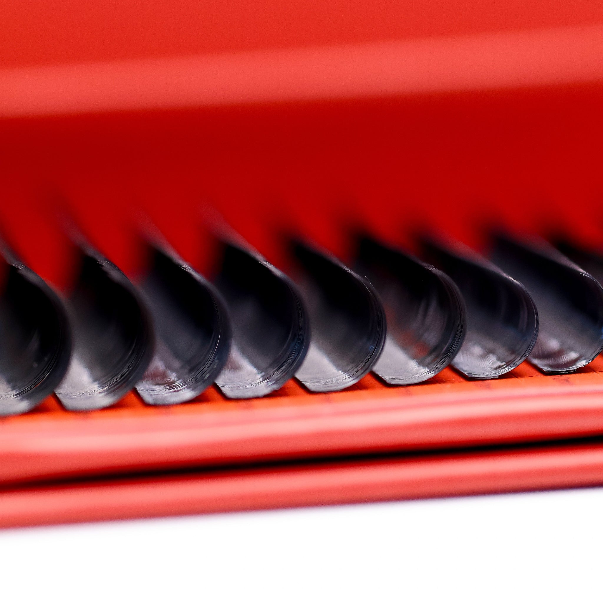 Ultra close-up of wet look lash extensions on red Ladybug Lashes tray showing defined glossy spike clusters and flat base structure
