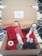 A lash starter kit with various tools and products displayed inside a cardboard box, including fans, glue, applicator wands, and a cooling jade stone.