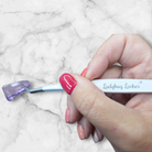 Hand holding a eyelash extension tool with 'Ladybug Lashes' branding on a marble background