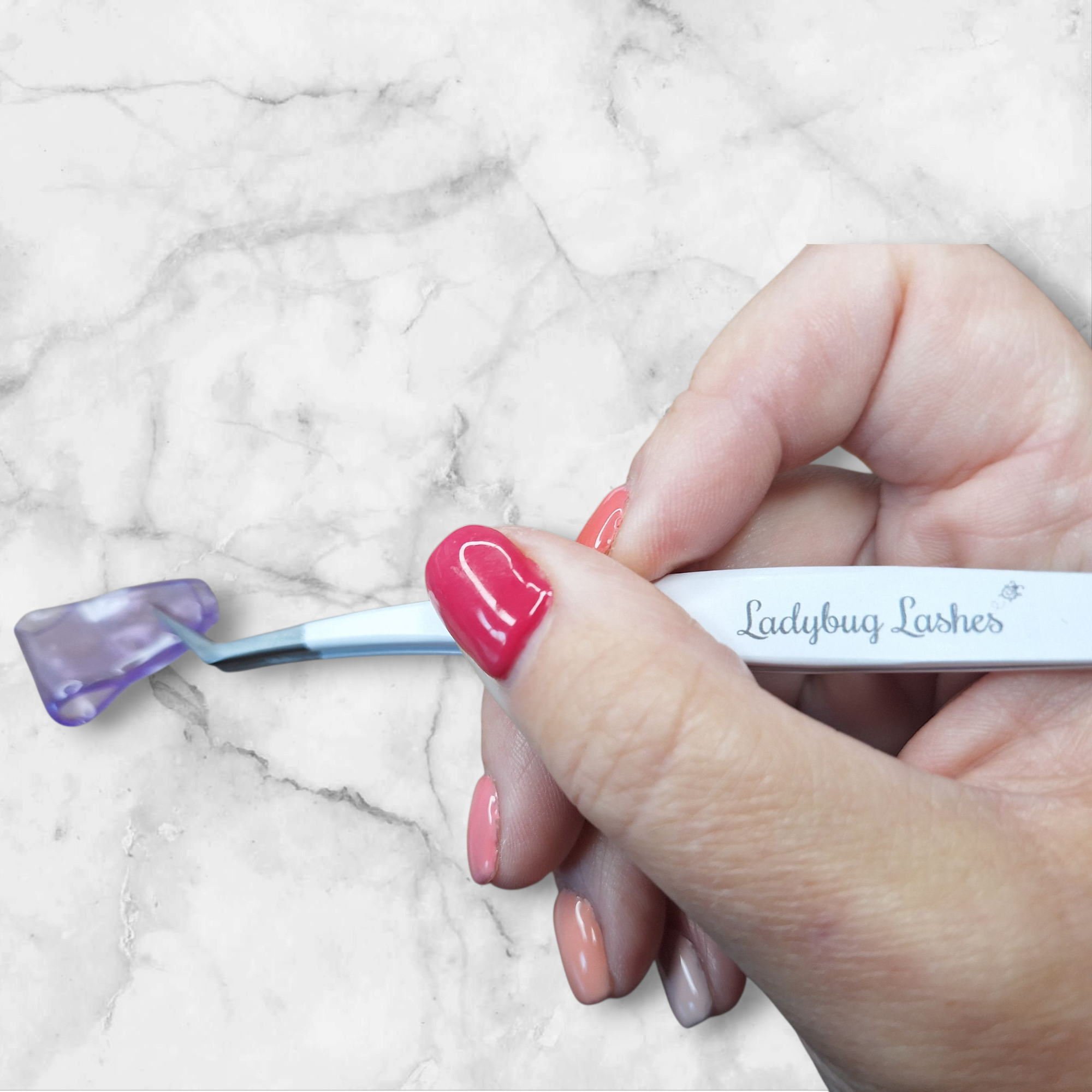 Hand holding a eyelash extension tool with 'Ladybug Lashes' branding on a marble background