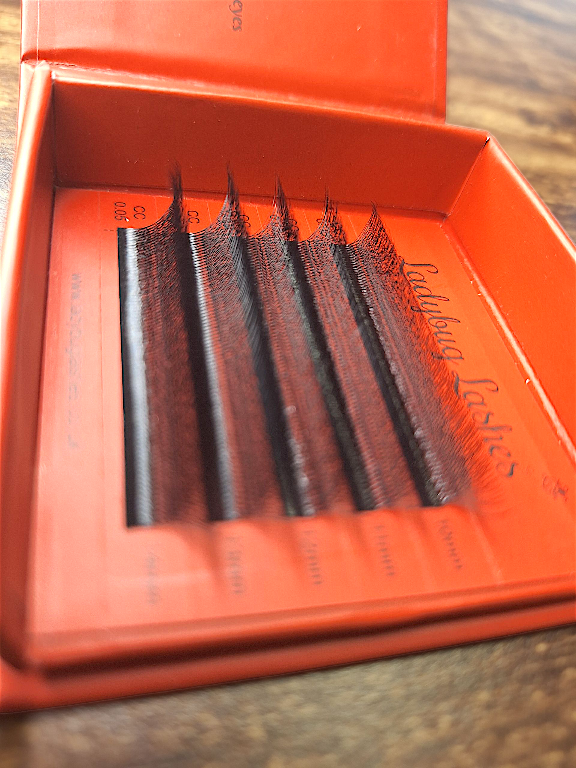 Open box of false eyelashes with visible branding on a wooden surface