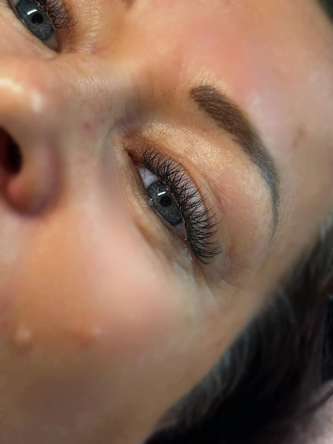 Close-up of a person's eye with applied false eyelashes, showcasing the 'W' lash extension design.