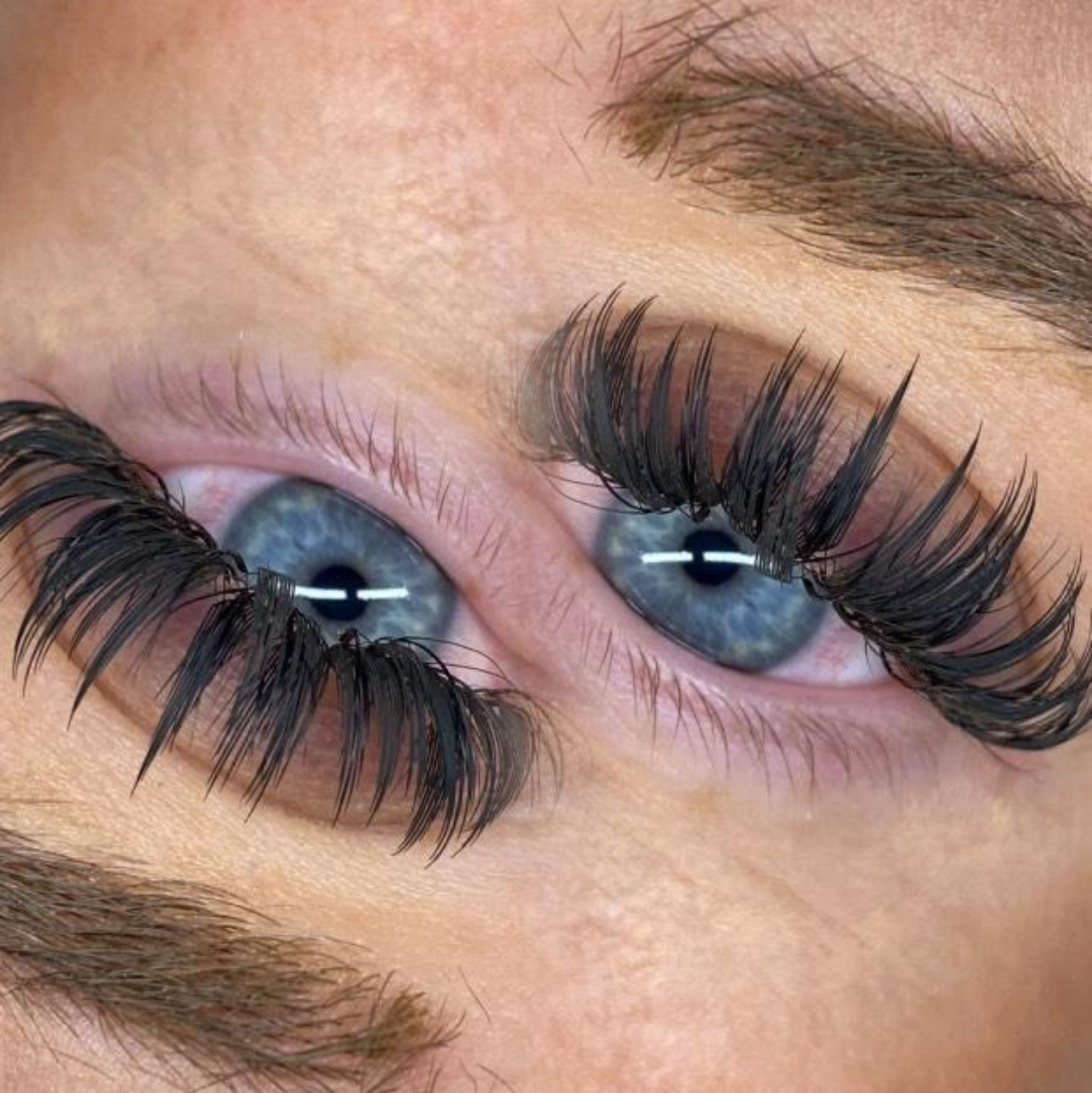 Overhead close-up of Anime Feather lash extension set on blue-grey eyes showing dramatic feather spike volume and wispy separation on both eyes