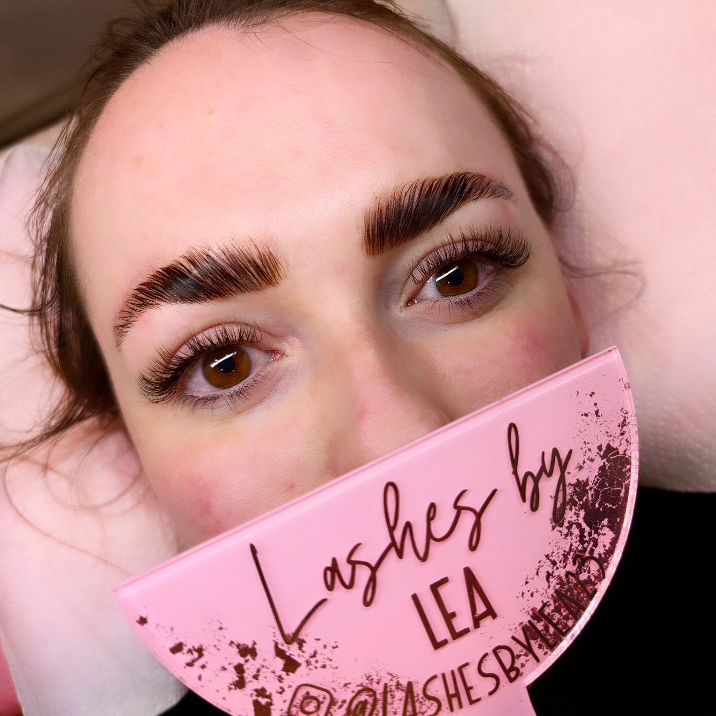 Person with applied eyelash extensions holding a pink tray.