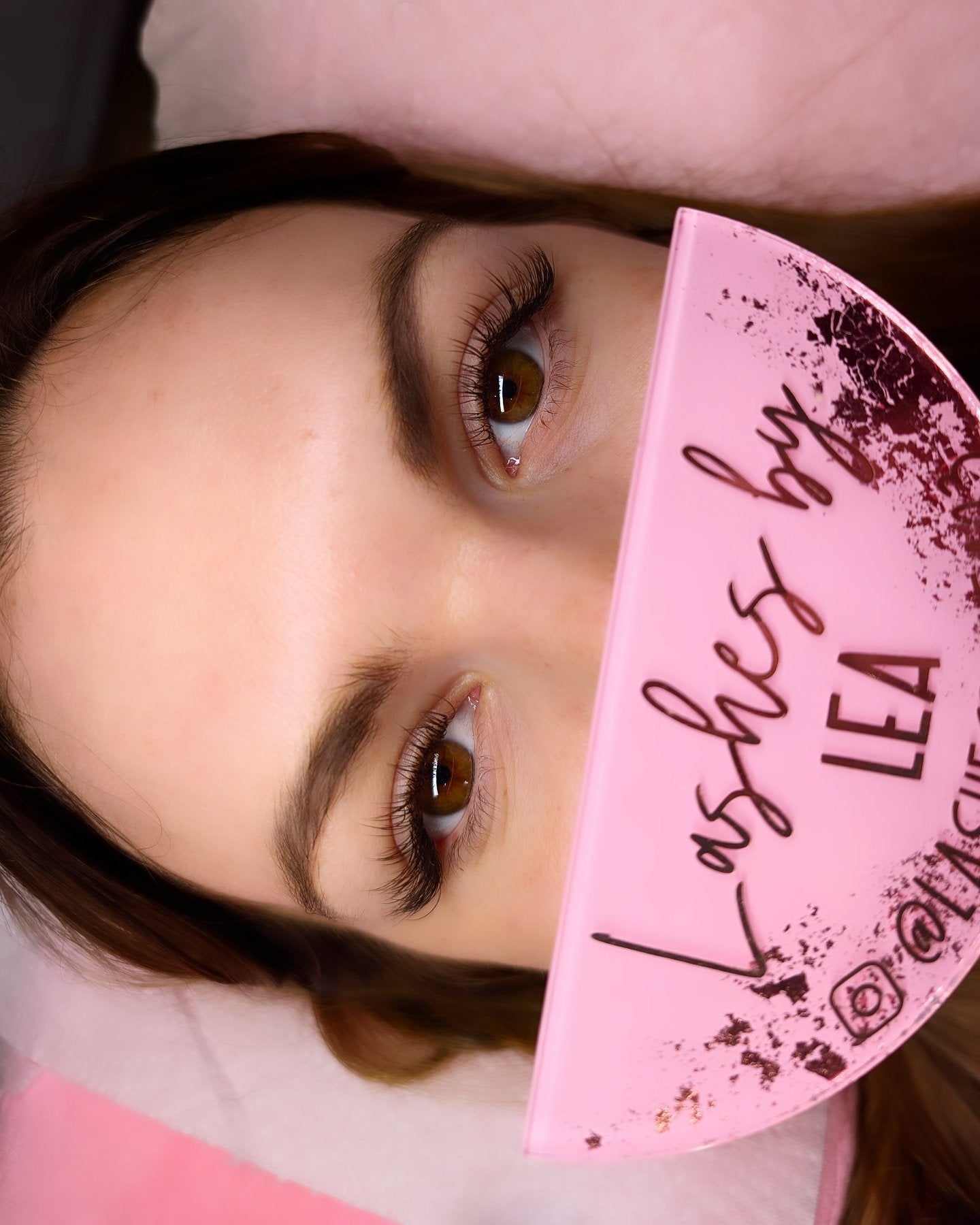 Close-up of eyes with pink lash product packaging.