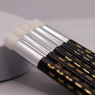 Ladybug Lashes Soft Bristle Lash Cleansing Brushes pack of 5 product shot showing five brushes fanned out in a row with white dome-shaped soft bristle heads silver ferrules and black handles printed with gold and white closed-eye lash motifs from diagonal overhead angle on white background