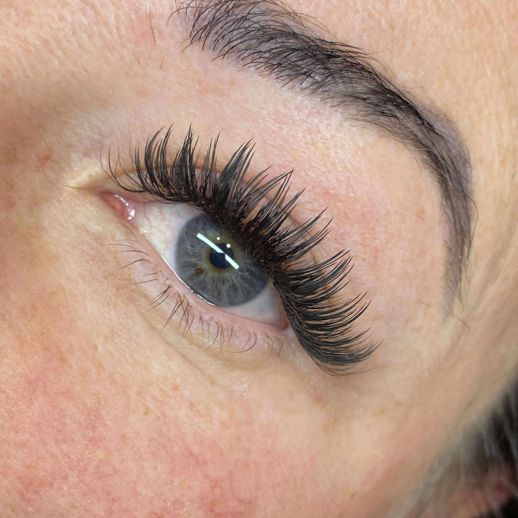 completed Anime Feather lash extension set on blue-grey eye showing soft feather spike volume from low upward angle