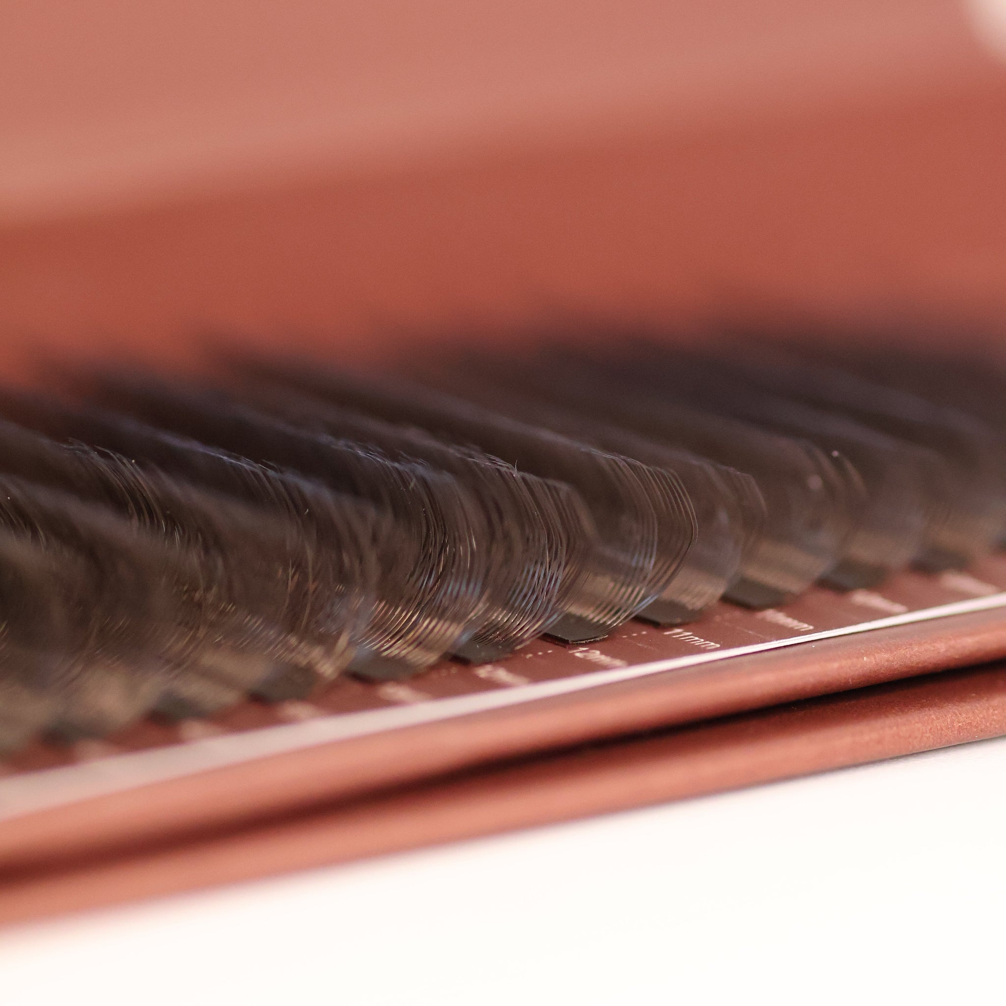 Extreme close-up side angle of brown W lash extensions on Ladybug Lashes tray showing W-shaped curl structure and warm brown tone