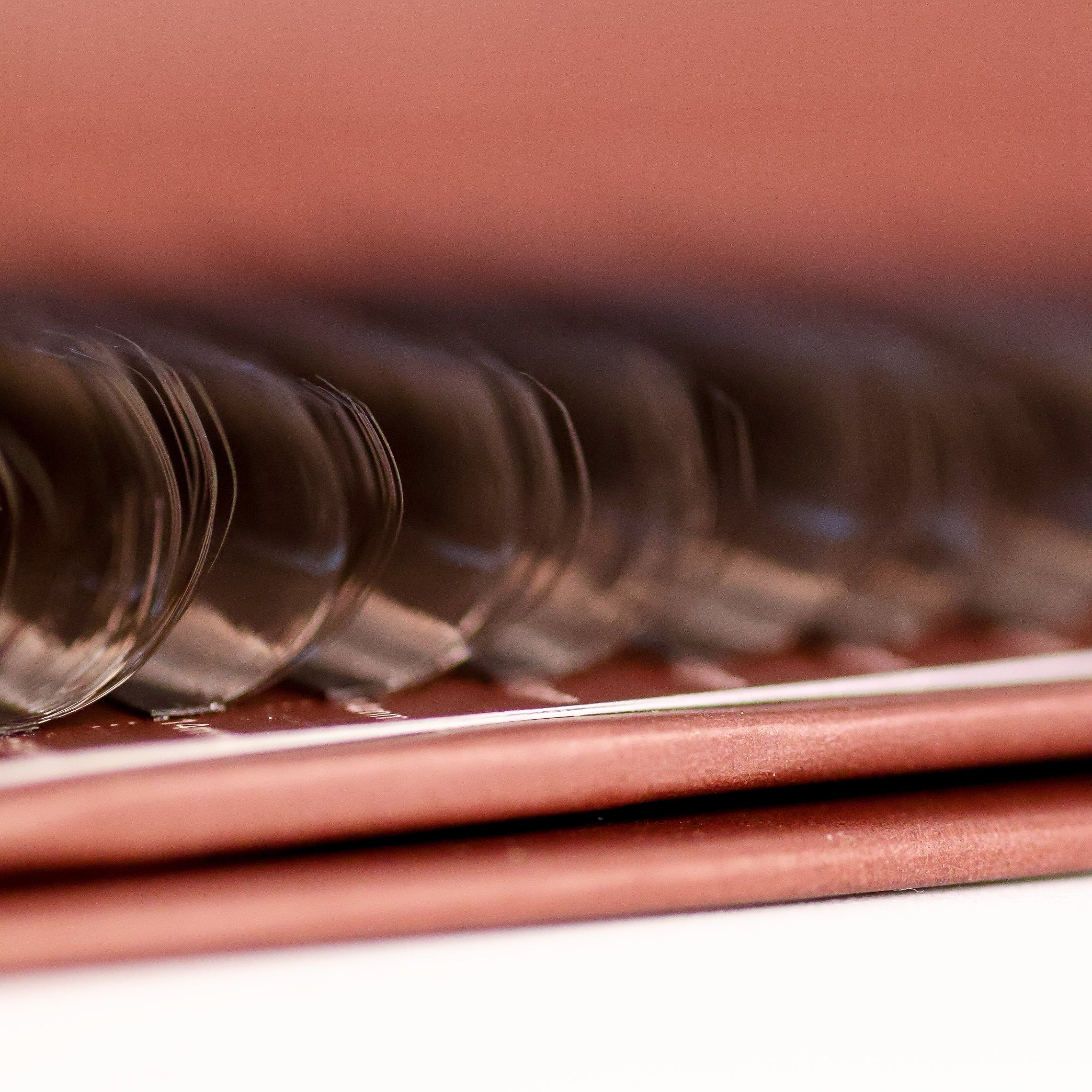 Extreme macro close-up of brown Fairy lash extensions on Ladybug Lashes tray showing rounded curl tips and soft brown tone from side angle