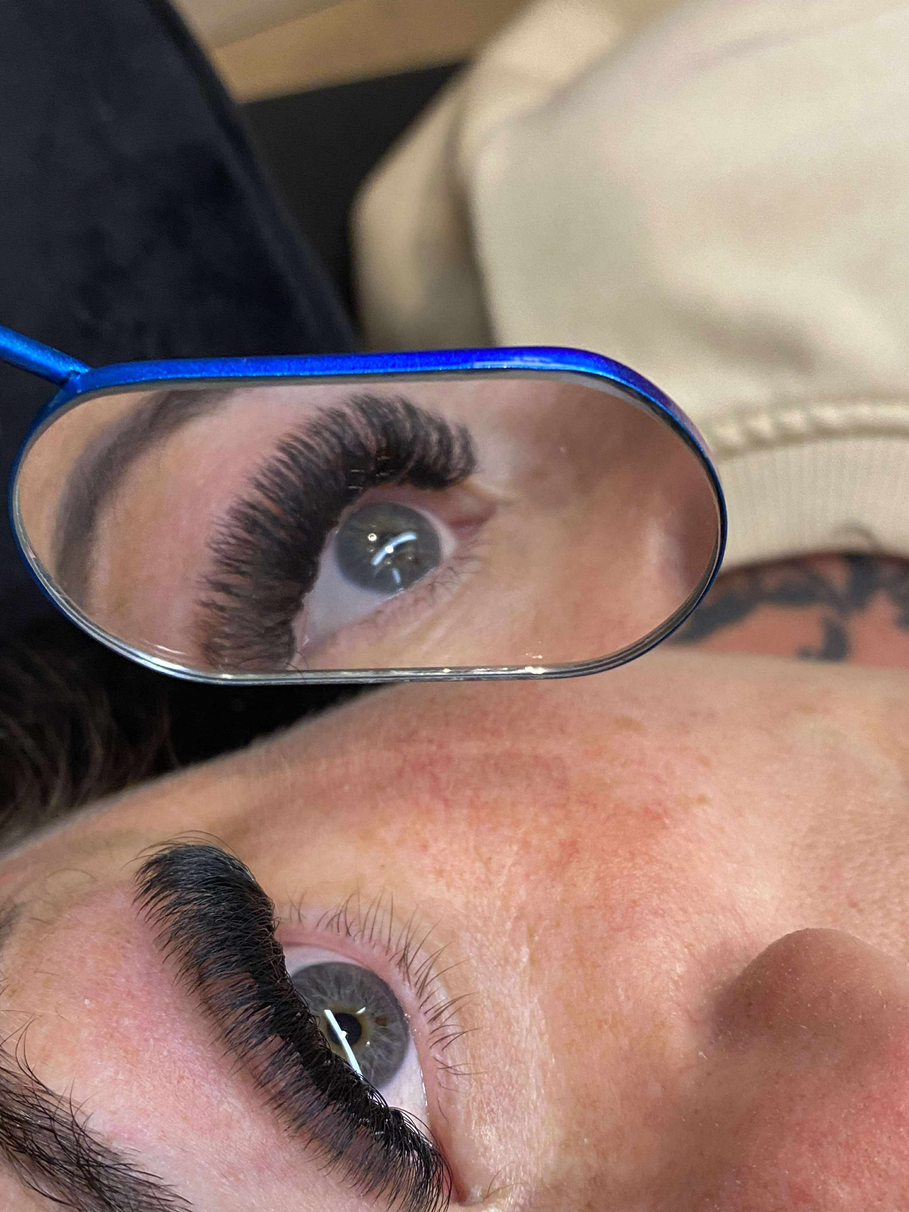Close-up of a person's eye with false eyelashes being applied using a small mirror.