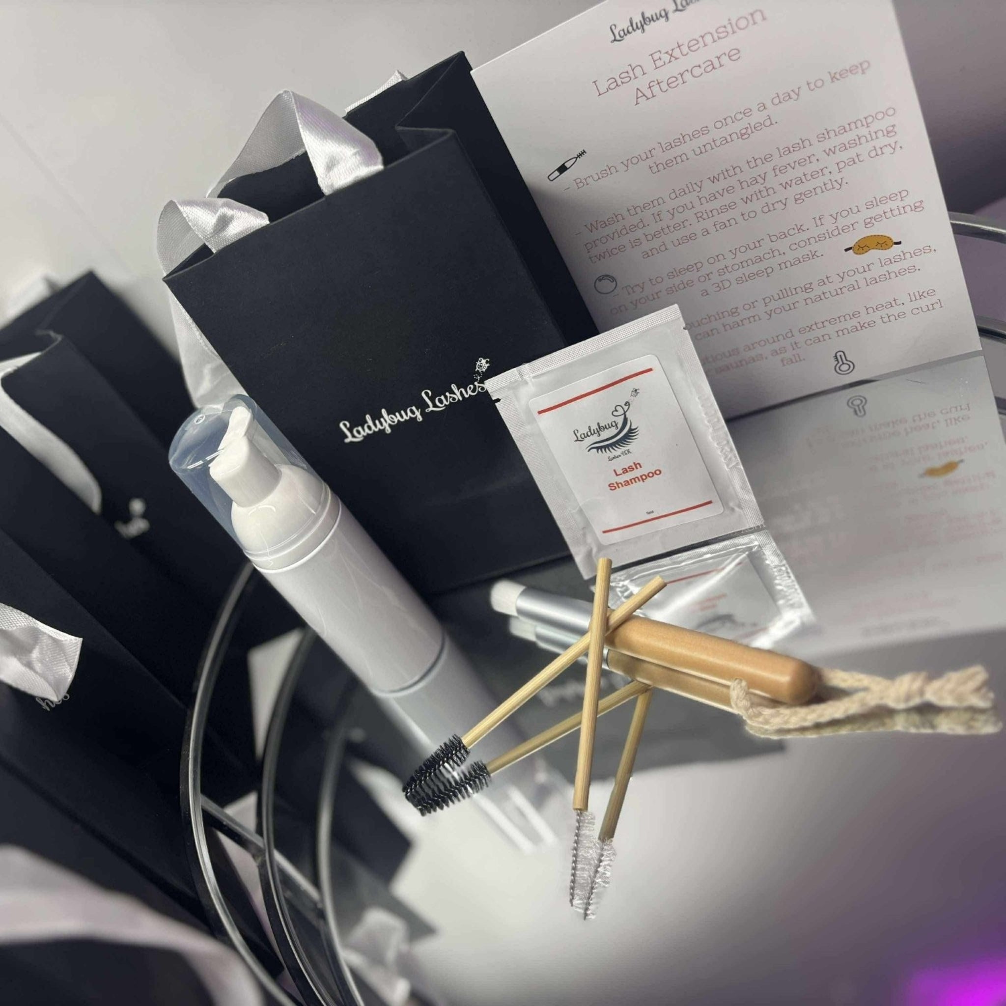 Multiple Ladybug Lashes Lash Shampoo Sachet Kits prepared and ready to hand out, showing several black Ladybug Lashes gift bags with white tissue paper lined up in a row, each containing a white foam pump bottle, lash shampoo sachet, bamboo spoolie, bamboo cleansing brush and aftercare card