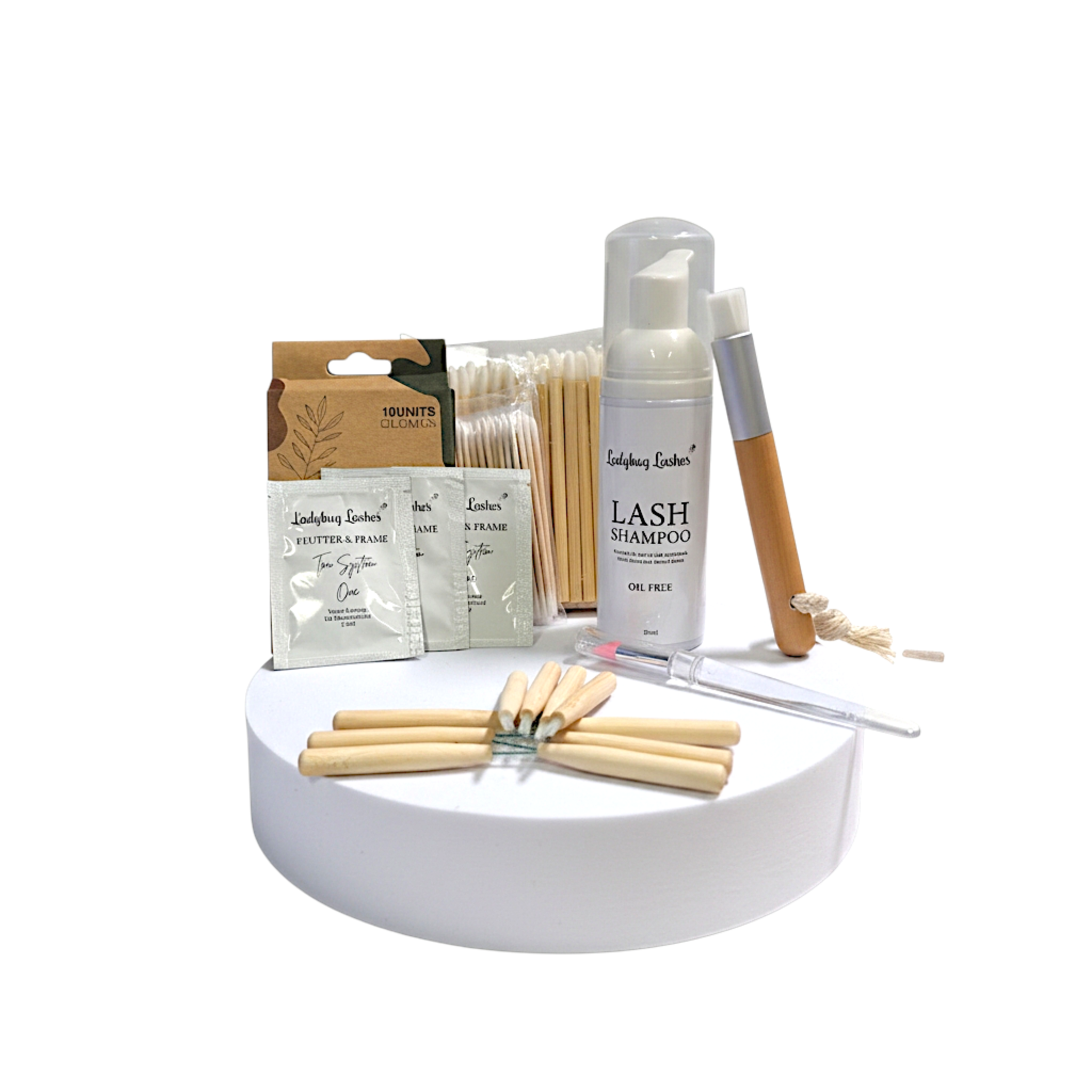 Ladybug Lashes Flutter and Frame Brow Lamination Sachet Kit flatlay product shot showing full kit contents including three Flutter and Frame sachets Ladybug Lashes oil-free lash shampoo foam pump wooden spatulas cotton buds disposable brushes glass dropper and brow rods arranged on white circular plinth on white background