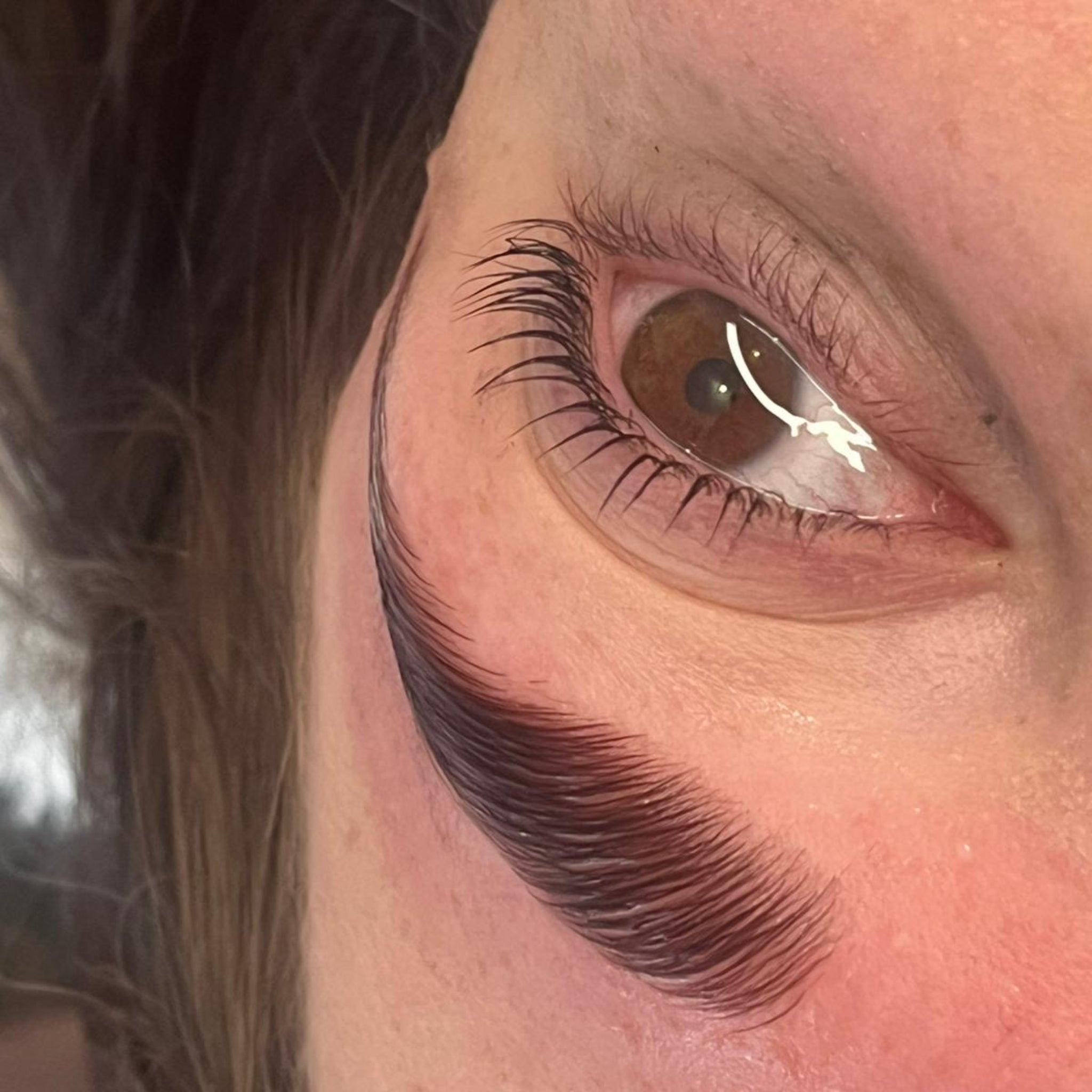 Ladybug Lashes Airless Pump Express Cysteamine Brow Lamination Kit close-up result shot showing lifted and curled lash extensions on open brown eye from diagonal angle with defined dark brow and natural skin texture visible