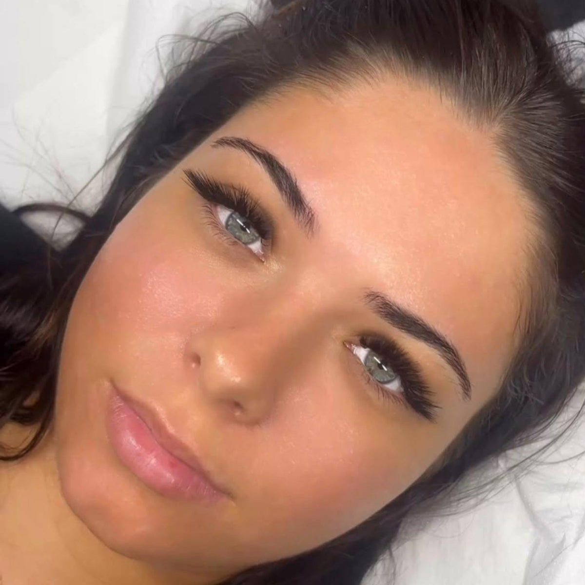 Front-facing close-up of model with blue-grey eyes showing completed Ladybug Lashes L curl volume lash extension set with dramatic lift and defined brow framing