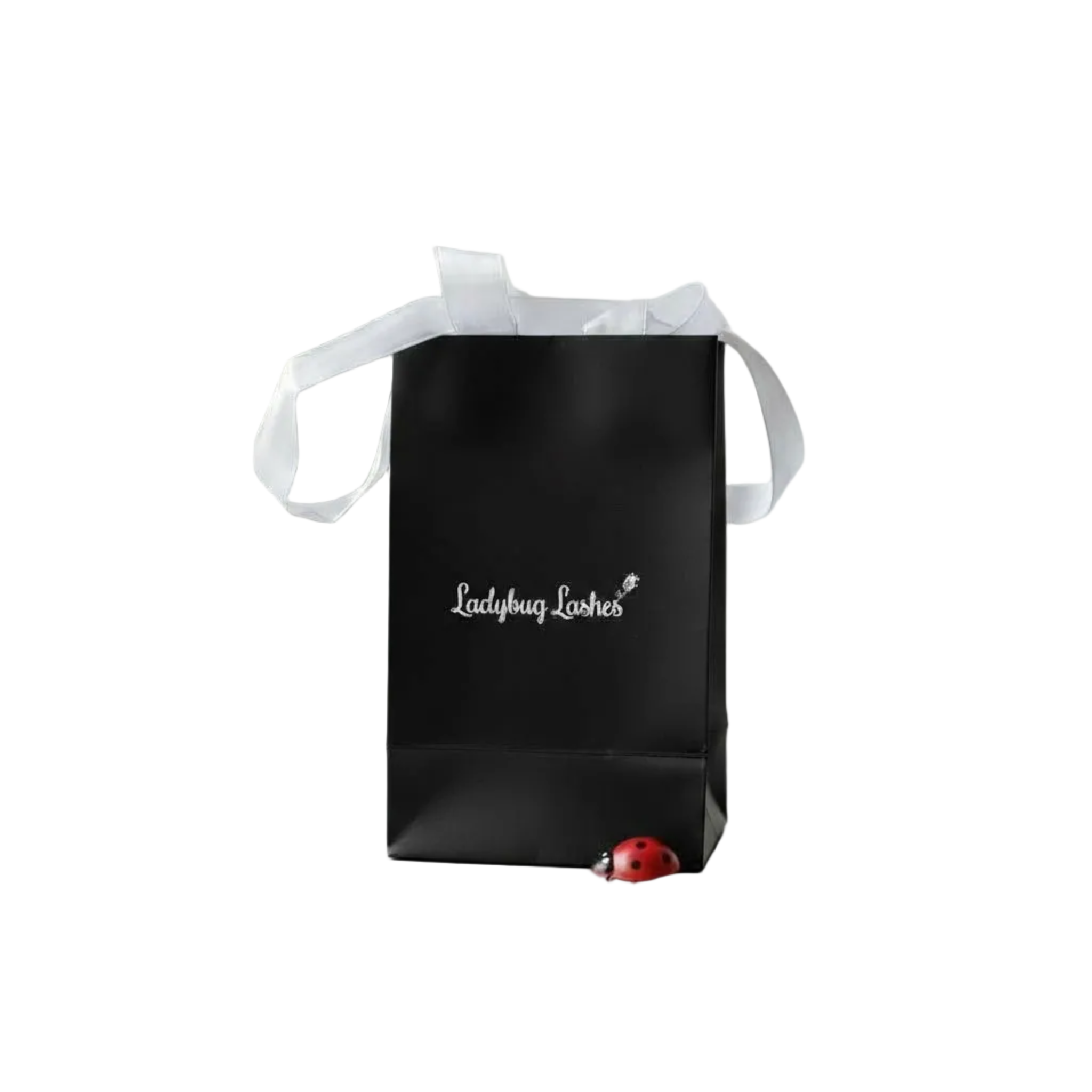 Matte black gift bag with white satin ribbon handles printed with "Ladybug Lashes" in silver script with a lash wand icon, and a small red and black ladybird ornament sitting at the base, displayed against a white background — sold as a pack of 5 for lash and brow aftercare or client gift packaging