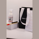 Ladybug Lashes Lash Shampoo Kit contents showing a Ladybug Lashes Bubblegum Shampoo 30ml foam pump bottle on a white plinth, a bamboo-handled lash cleansing brush with red spoolie, a black Ladybug Lashes gift bag with white ribbon handles and a printed Lash Extension Aftercare card on a white surface