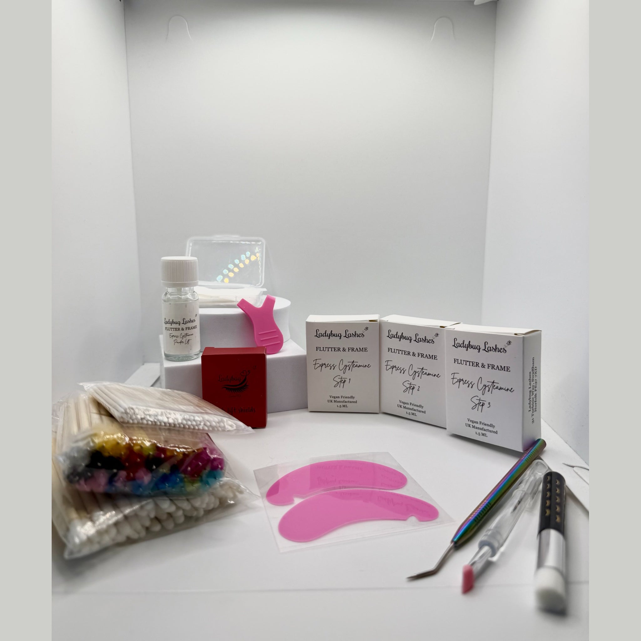 Ladybug Lashes Express Cysteamine Lash Lift Sachet Kit product shot showing Flutter and Frame Step 1, 2 and 3 sachet boxes, treatment bottle, pink lash lift tool, silicone under eye pads, cotton buds, rainbow mascara wands, microfibre brushes and tweezers on white background