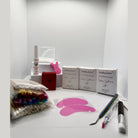 Ladybug Lashes Express Cysteamine Lash Lift Sachet Kit flatlay showing Flutter and Frame Step 1, 2 and 3 sachet boxes, Bonder bottle, pink lash lift tool, silicone under eye pads, rainbow mascara wands, microfibre brushes, tweezers and disposable applicators on white background