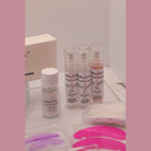 Close-up of open Ladybug Lashes Hybrid Lash Shields box showing pink silicone shields, Ladybug Lashes cling film dispenser box, Powder Lift bottle, coloured fine detail brushes and pink silicone lash shields in the foreground on a white surface
