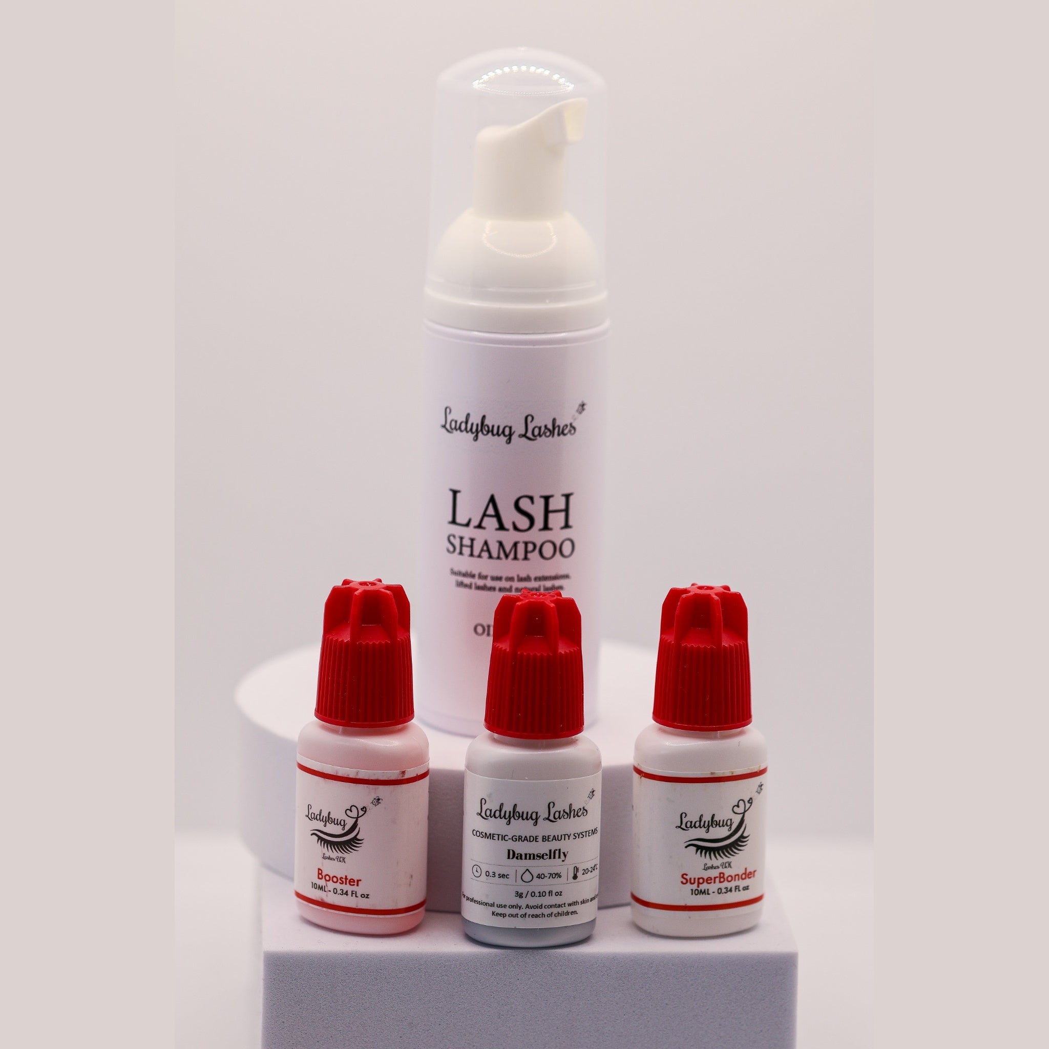 Ladybug Lashes Low Humidity Retention Trio showing four products on a white background: Lash Shampoo 50ml foam pump bottle, Booster 10ml bottle with red cap, Meadow adhesive 1g bottle with red cap, and SuperBonder 10ml bottle with red cap