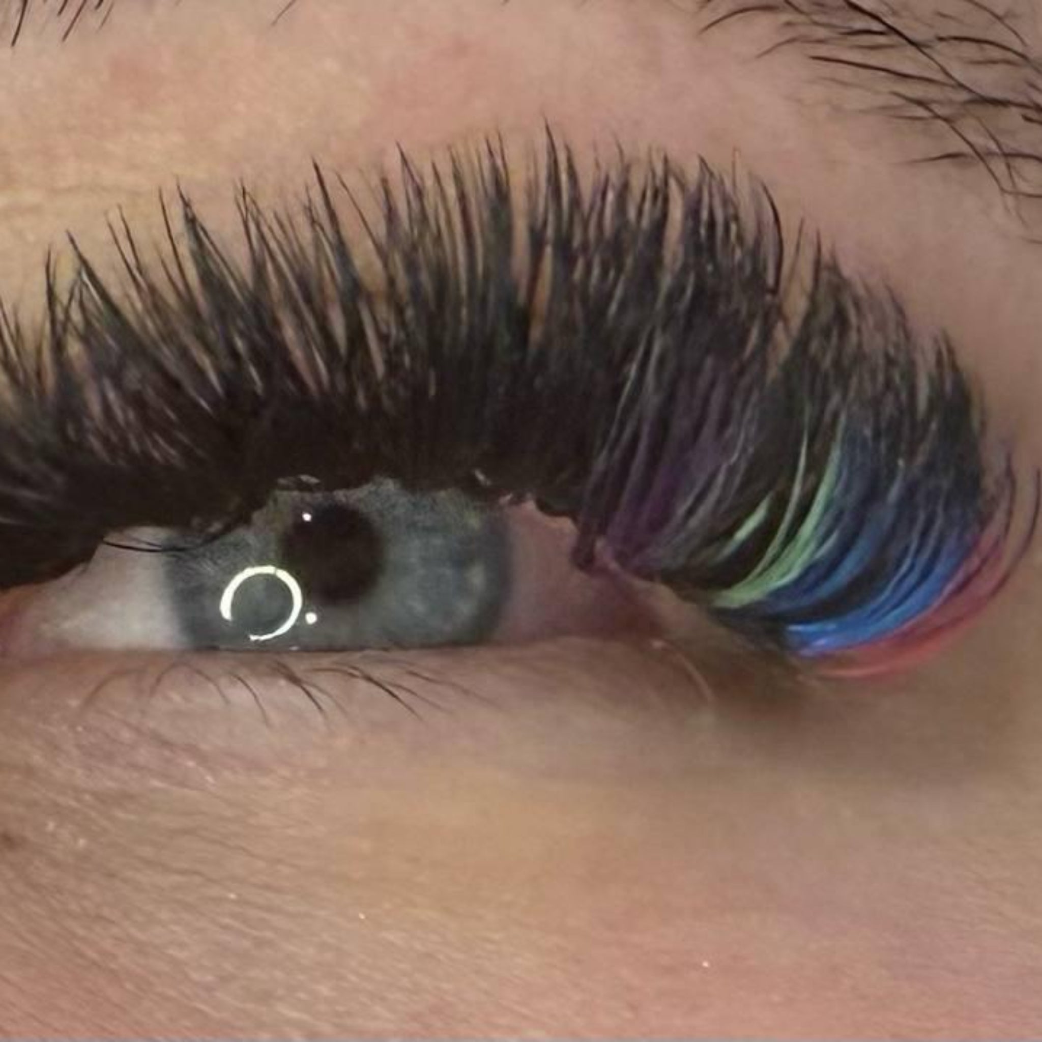 Ladybug Lashes Colour Volume Lashes application result extreme close-up showing open grey-green eye of a fair-skinned client wearing black volume lash extensions with multi-coloured tips at the outer corner from diagonal angle
